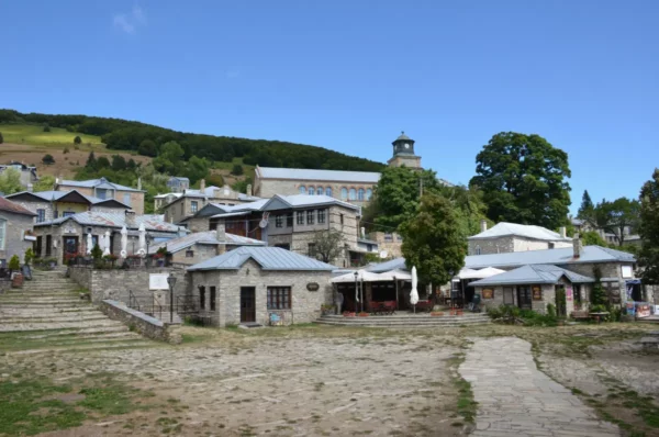 Stone-built houses and the central square of Nymfaio mountain village in Florina, northern Greece, with traditional Macedonian architecture and forested hills in the background.