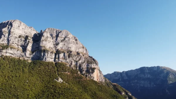 Stunning limestone cliffs rise dramatically against a clear blue sky in Papigo, Zagorochoria, Ioannina, Greece.