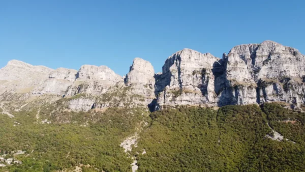 Majestic rocky cliffs rise against a clear blue sky in Papigo, Zagorochoria, showcasing the natural beauty of Ioannina, Greece.