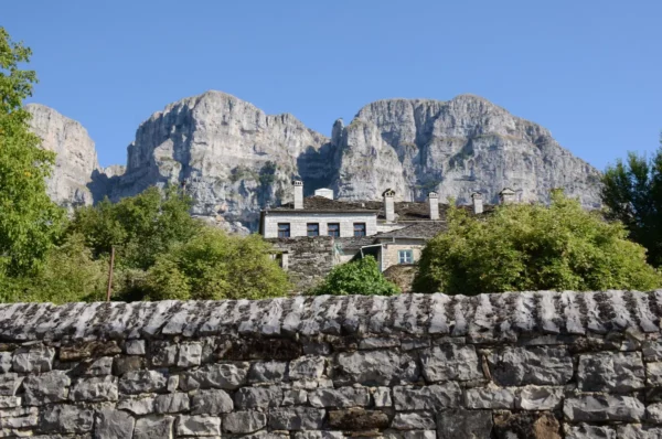 Stone houses in Papigo village, Zagorochoria, framed by dramatic limestone cliffs of Mount Tymfi under clear summer light.