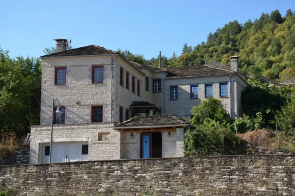 Charming stone house with red windows surrounded by lush greenery in Papigo, Zagorochoria, Ioannina, Greece.