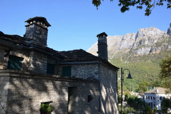 Traditional stone architecture with green shutters, set against a backdrop of steep mountains in Papigo, Zagorochoria, Ioannina, Greece.
