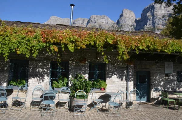 Quaint café in Papigo, Zagorochoria, with a vine-covered facade and tables overlooking stunning mountain views.