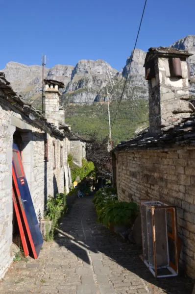 Charming stone houses line the narrow path in Papigo, Zagorochoria, with impressive mountain peaks rising in the background.