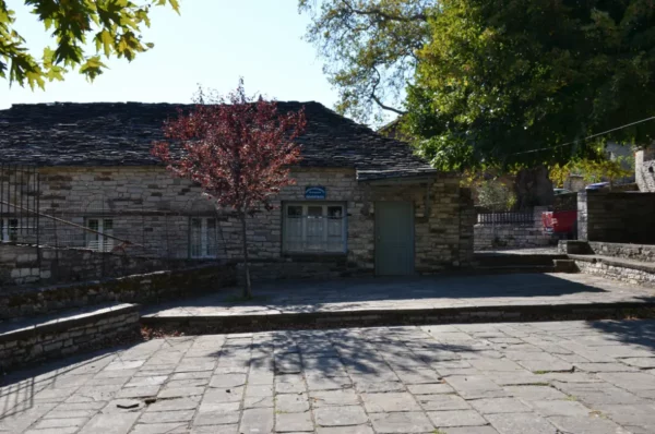 Traditional stone house with a slate roof, surrounded by grassy areas and trees in Papigo, Zagorochoria, Ioannina, Greece.
