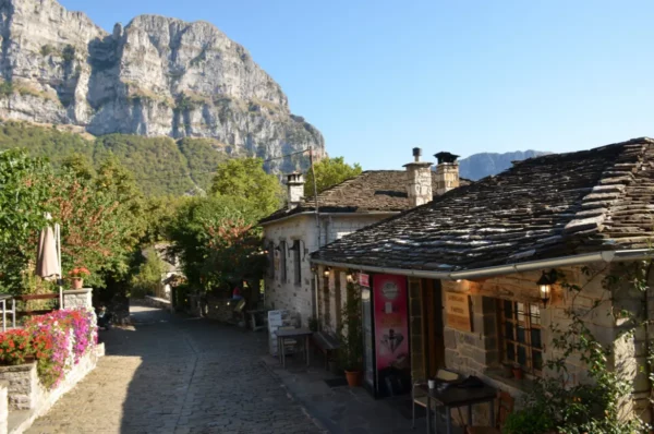 Stone-built houses and cobbled lane in Papigo village, Zagorochoria, Epirus, with limestone cliffs rising behind on a clear summer day.