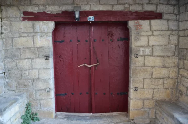 Rustic red wooden doors with iron straps, set against a stone wall in Papigo, Zagorochoria, Ioannina, Greece.
