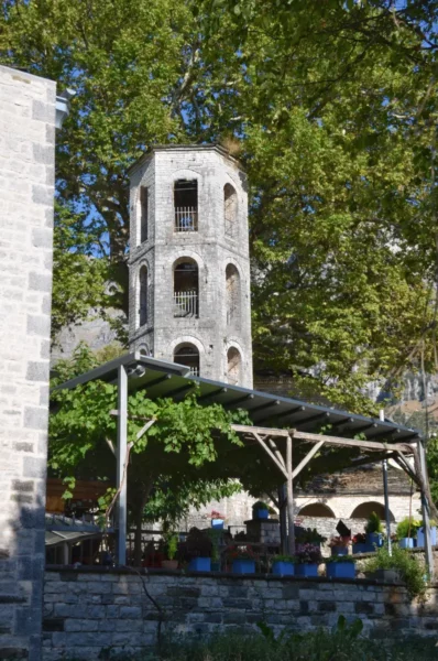 Historic stone tower amidst lush greenery in Papigo, Zagorochoria, showcasing local architecture and vibrant outdoor seating.
