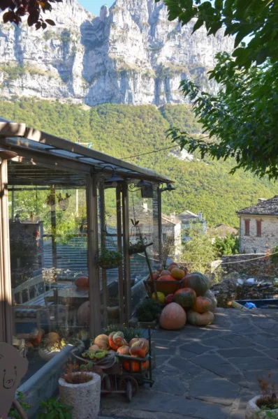 Colorful pumpkins and gourds are displayed in a quaint stone courtyard, framed by towering mountains in Papigo, Zagorochoria, Greece.