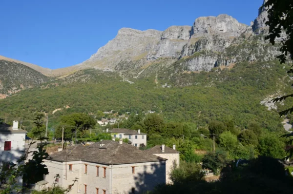 Stunning mountains rise above the lush greenery and traditional stone houses in Papigo, Zagorochoria, Ioannina, Greece.