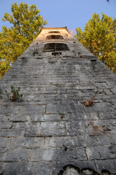 Ancient stone bell tower surrounded by lush trees in Papigo, Zagorochoria, Ioannina, Greece. Clear blue sky above.