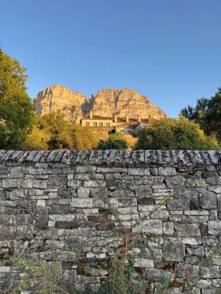 Sunlit stone wall at Papigo, with rocky mountains and lush greenery of Zagorochoria, Ioannina, Greece in the background.