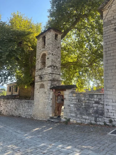 Charming stone tower with a clock in Papigo, Zagorochoria, surrounded by lush greenery and cobblestone pathways.