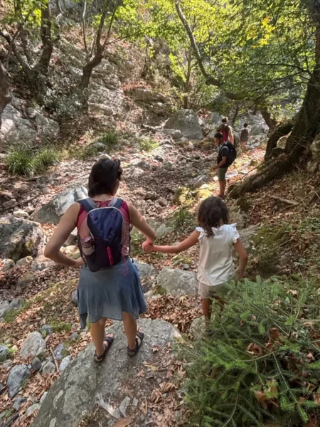 Hikers navigate the rocky trail through lush greenery in Stropones Gorge, Euboea, Greece, surrounded by vibrant autumn foliage.