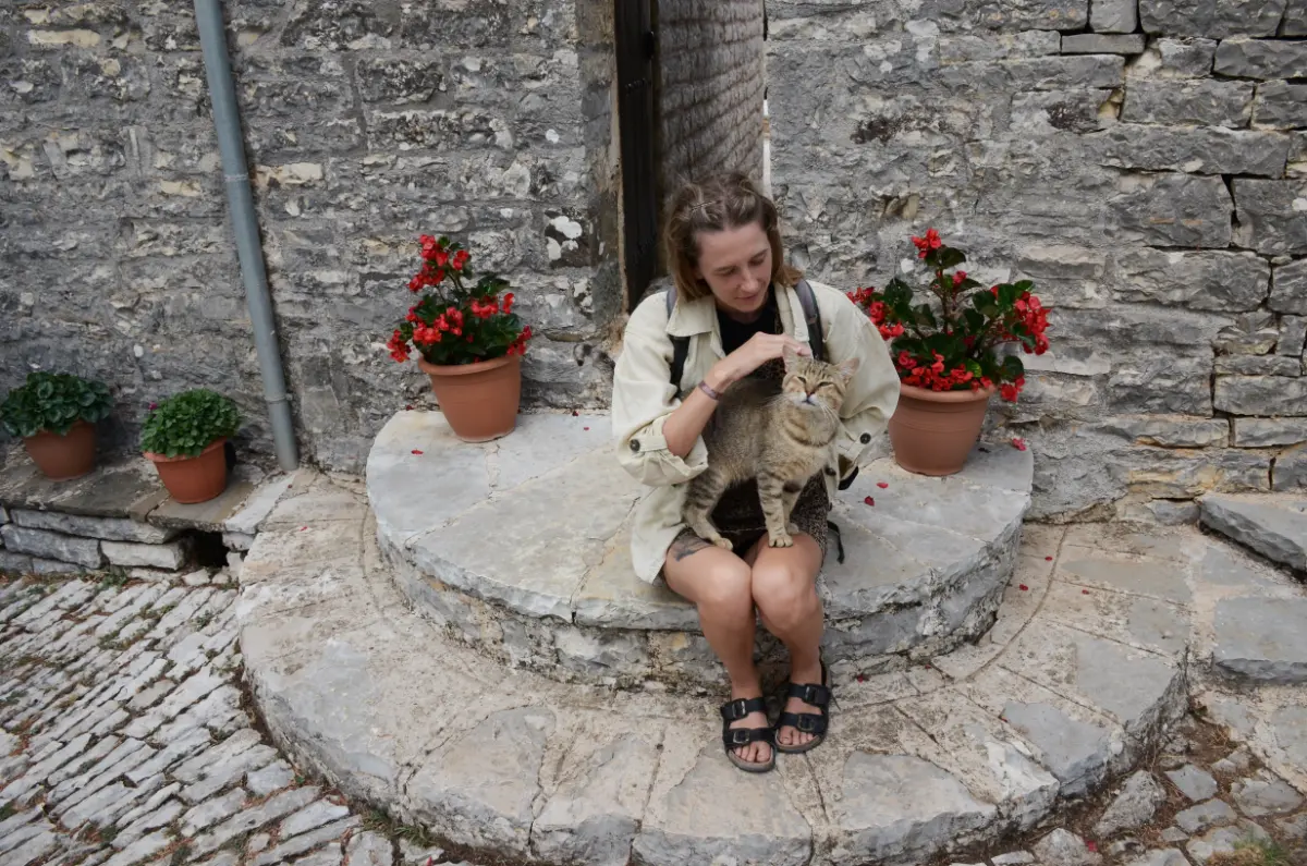 girl cozying up with cat in courtyard of tsouka monastery in elliniko, tzoumerka, greece
