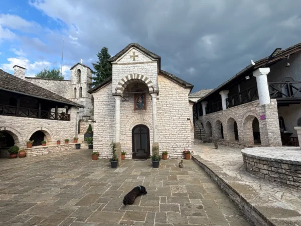 Tsouka Monastery courtyard in Elliniko, Tzoumerka, Epirus — stone church, arches, and quiet mountain setting