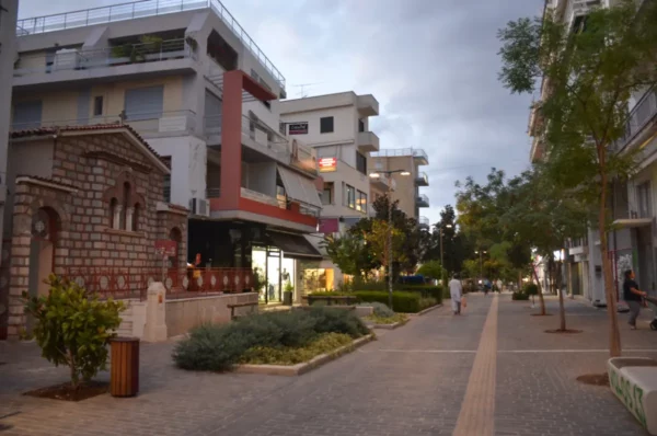 Charming streets of Thebes, Boeotia, Greece, featuring lush greenery, modern buildings, and historical architecture lining the walkway.