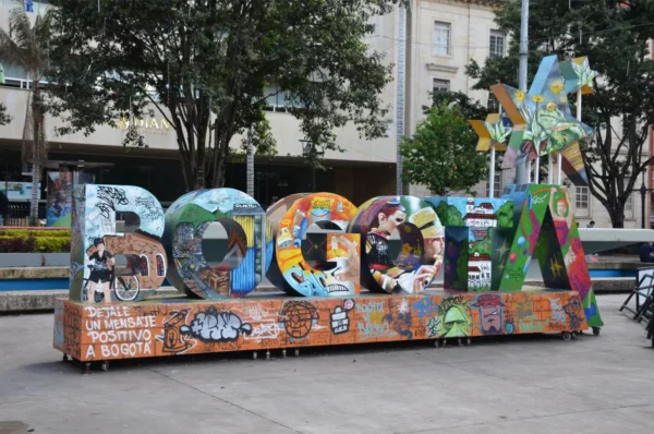 Colorful "Bogotá" sign in Santander Park surrounded by trees and modern buildings