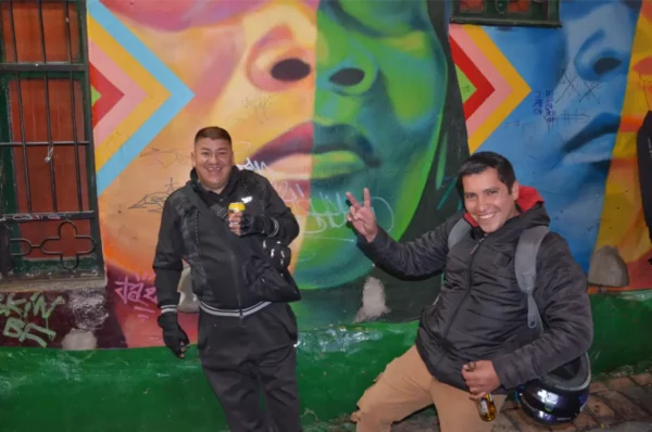 Two men posing in front of a colorful street art mural in La Candelaria, Bogotá