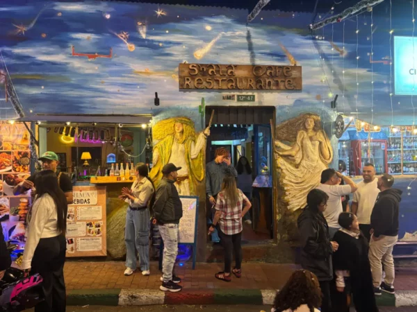 Bar entrance decorated with colorful murals and string lights in La Candelaria, Bogotá, with people gathered outside