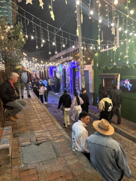 Busy nightlife street in La Candelaria, Bogotá, with bars, colorful façades, and crowds beneath festive lights