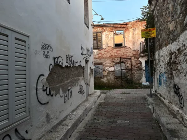 Chalkis features narrow streets with whitewashed walls, graffiti, and a glimpse of an old, crumbling building in Euboea, Greece.