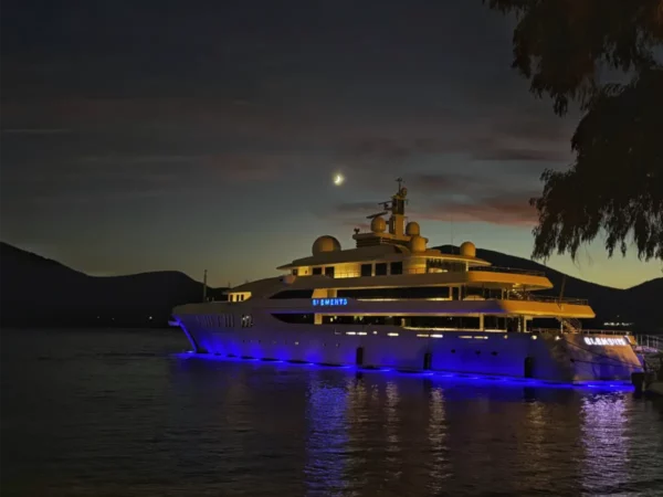 Luxury yacht illuminated in blue lights docked in Chalkis, Euboea, Greece, under a crescent moon and a twilight sky.
