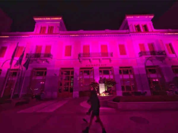 Vibrant pink lights illuminate a historic building in Chalkis, Euboea, creating a striking night scene with a pedestrian passing by.