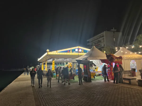Vibrant night market in Chalkis, Euboea, Greece, featuring colorful stalls, glowing lights, and people enjoying the atmosphere.