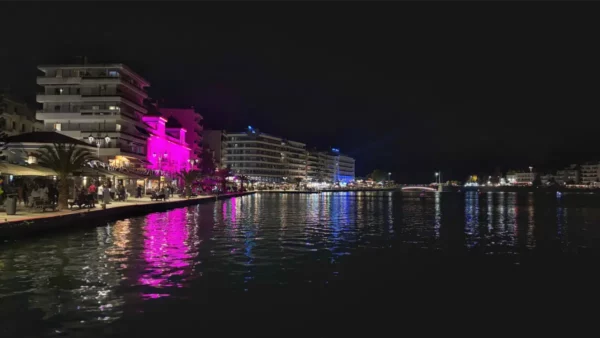 Vibrant lights reflect on the water in Chalkis, Euboea, Greece, showcasing a lively waterfront scene at night.
