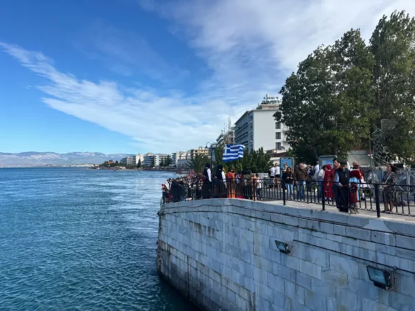Clear blue skies and calm waters frame a lively waterfront scene in Chalkis, Euboea, Greece, with people enjoying the view.