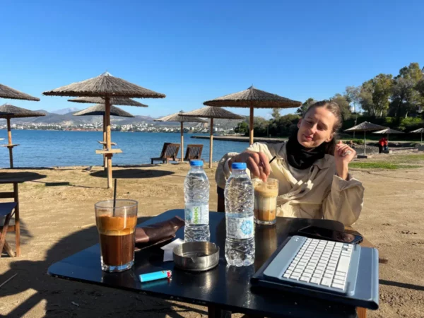 Chilling by the beach in Chalkis, Euboea, with iced coffee, water bottles, and a laptop under straw umbrellas.
