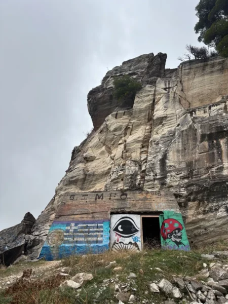 Davelis Cave features vibrant graffiti on its entrance against the rugged cliffs of Mount Pentelicus, Attica, Greece.