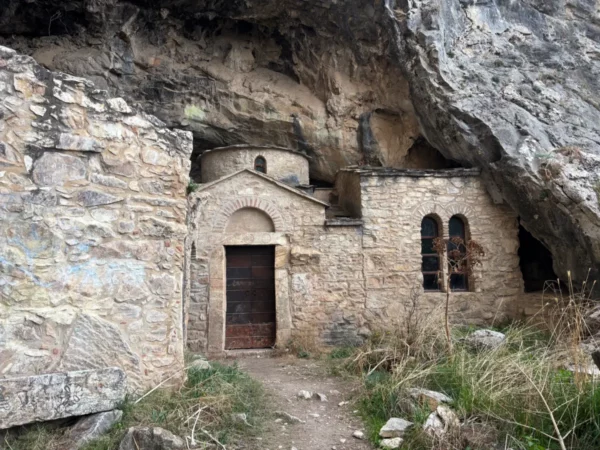 Davelis Cave features ancient stone structures nestled under a rocky overhang in Mount Pentelicus, Attica, Greece.