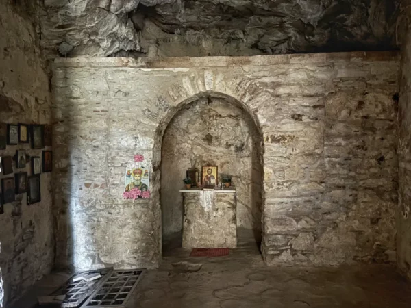 Davelis Cave features rough stone walls, an arched niche with candles and icons, and historic photographs adorning the walls in Mount Pentelicus, Attica, Greece.