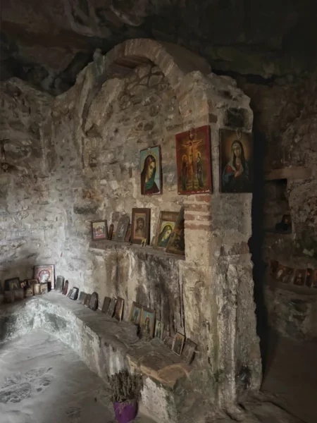 Davelis Cave features a stone wall adorned with religious icons, illuminated softly in the dimly lit interior of Mount Pentelicus, Attica.