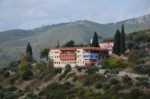 Makrymalli Monastery in Euboea, Greece, nestled among rolling green hills, features rustic buildings and lush olive trees.