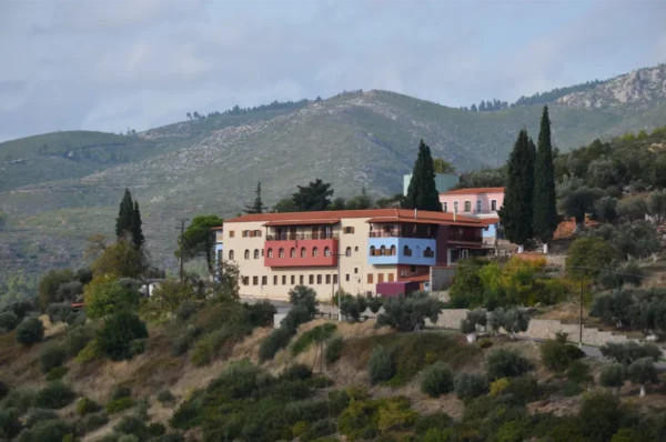 Makrymalli Monastery in Euboea, Greece, nestled among rolling green hills, features rustic buildings and lush olive trees.