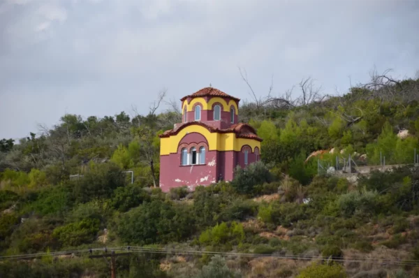 colorful chapel near Makrymalli Monastery nestled among lush greenery on Euboea, Greece, with a picturesque sky in the background.