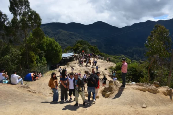 Visitors gather on the scenic path to Monserrate, surrounded by lush greenery and distant mountains under a partly cloudy sky.