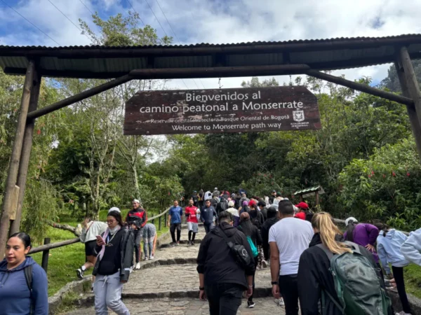 Hikers climbing the stone steps of the Monserrate trail beneath the welcome sign at the entrance in Bogotá
