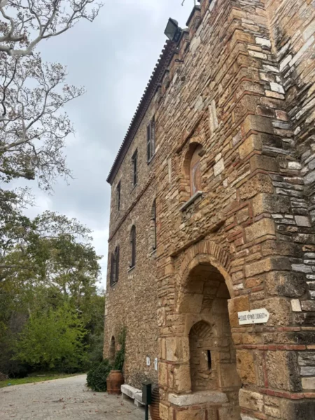 Stone exterior of Penteli Monastery in Attica, Greece, showcasing rough textures and natural surroundings under a cloudy sky.