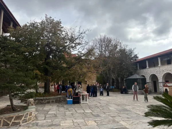 Visitors gather in the stone courtyard of Penteli Monastery in Attica, Greece, surrounded by trees and historic architecture.