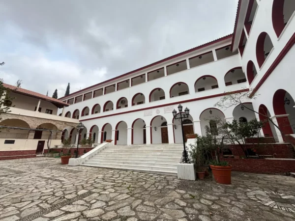 Penteli Monastery features a spacious courtyard with white arches and stone pathways, framed by lush greenery in Attica, Greece.