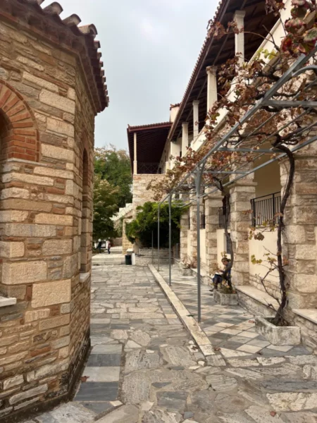 Stone pathway leading past weathered walls and pillars at Penteli Monastery, surrounded by greenery in Attica, Greece.