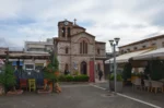 Charming church with stone architecture situated in a lively square in Psachna, Euboea, Greece, surrounded by colorful dining areas.