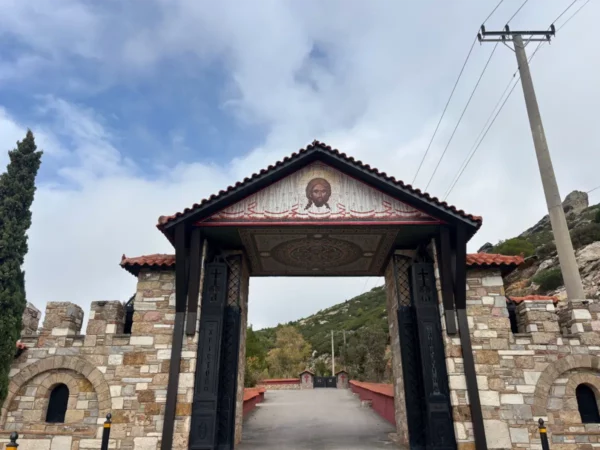 Saint Panteleimon Monastery's entrance features stone walls and a tile roof, set against the backdrop of Mount Pentelicus in Attica, Greece.