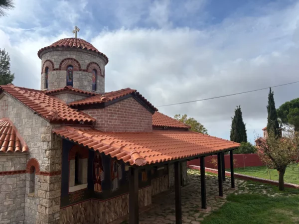 Saint Panteleimon Monastery features a stone façade and red-tiled roof, surrounded by greenery on Mount Pentelicus, Attica, Greece.
