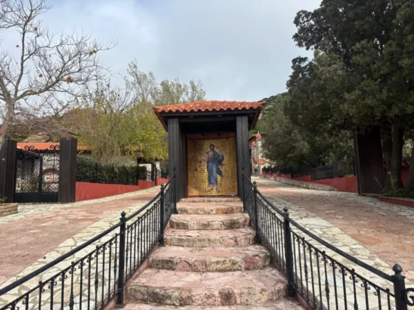 Stairs lead to an entrance with religious iconography, surrounded by trees and a serene pathway at Saint Panteleimon Monastery, Mount Pentelicus.