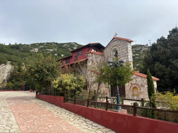 Saint Panteleimon Monastery features stone architecture framed by lush greenery and a cobblestone pathway on Mount Pentelicus, Attica.